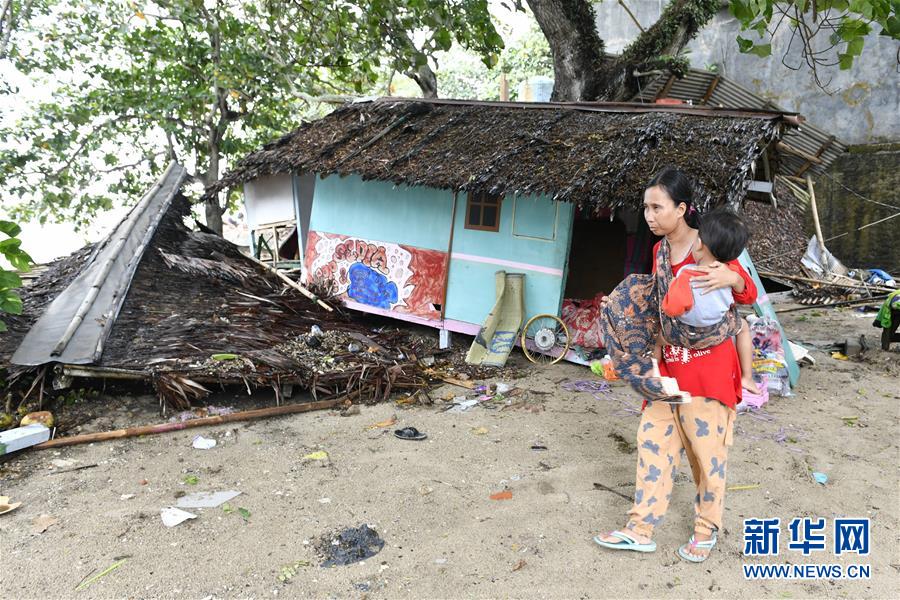 12月23日，在印度尼西亚万丹省卡里塔，一名女子抱着孩子从一处建筑残骸旁走过。 印度尼西亚抗灾署23日说，印尼西部巽他海峡海啸死亡人数已经上升到168人。印尼西部巽他海峡22日晚发生海啸。海啸发生时当地没有监测到地震活动，初步怀疑海啸是由喀拉喀托火山喷发引发海底岩层滑坡和月圆引发涨潮共同所致。 新华社发（韦宁摄）