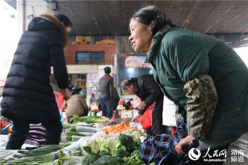 李新彩正在菜市场买菜。